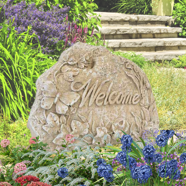 "Welcome" stone placed in a vibrant garden bed with flowers and greenery.